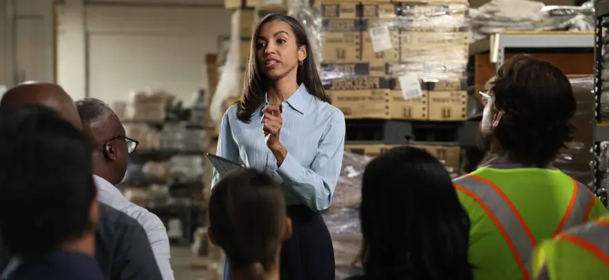 タブレットを持ち、倉庫にいる従業員の前で話す女性