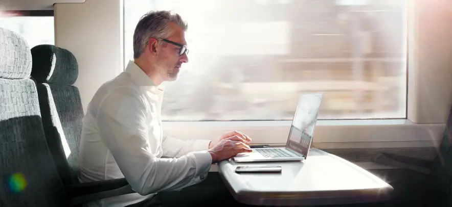 電車乗車中にコンピューターで作業する男性